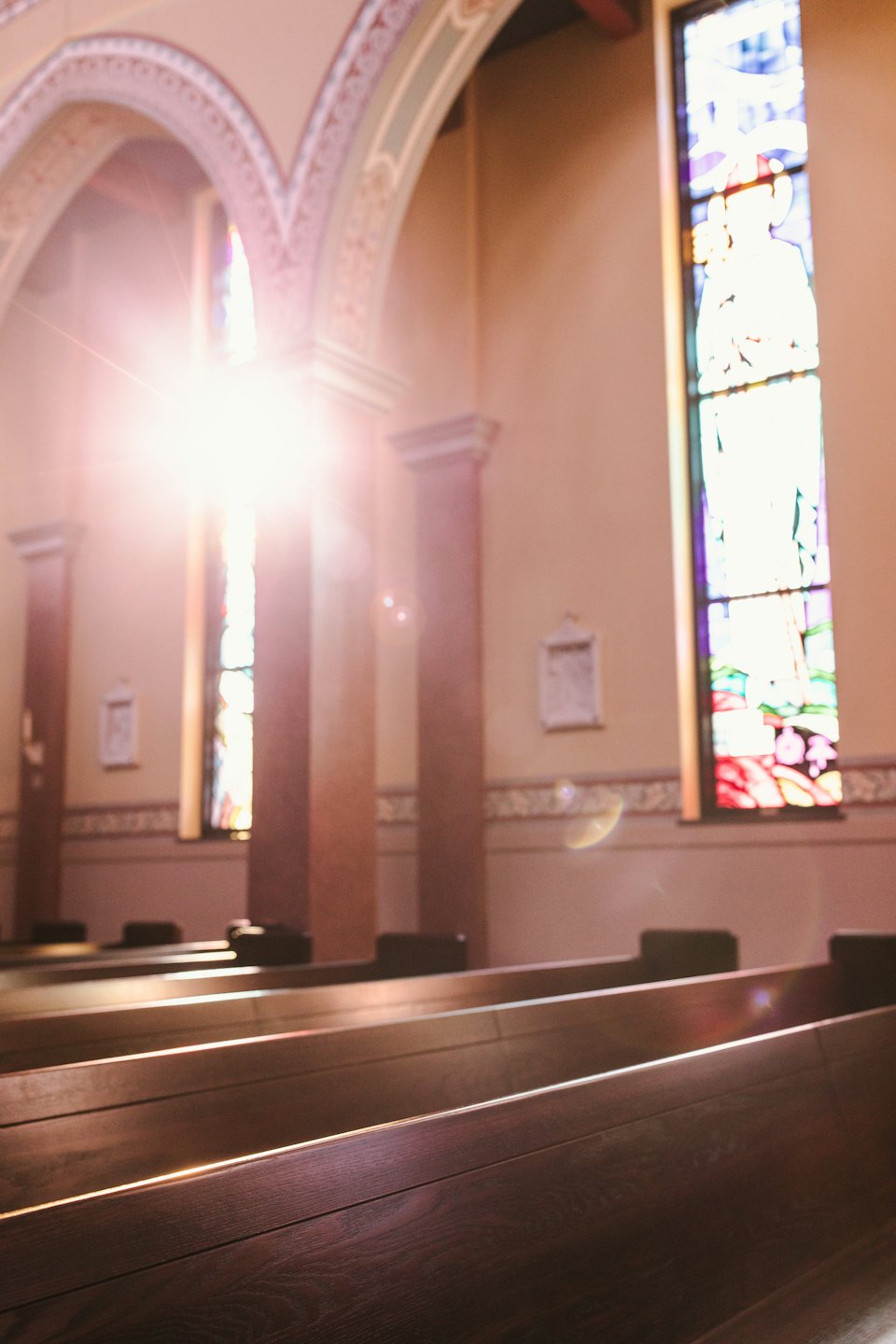 Sunlight streams through a stained-glass window onto church pews.