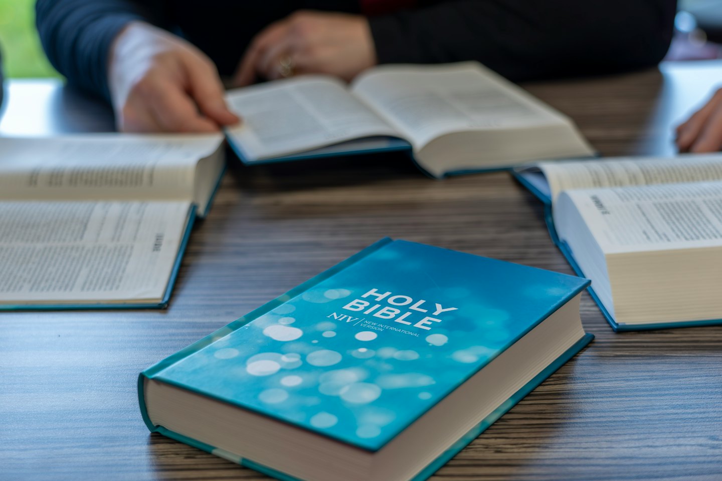 Two people read open Bibles together on a wooden table.